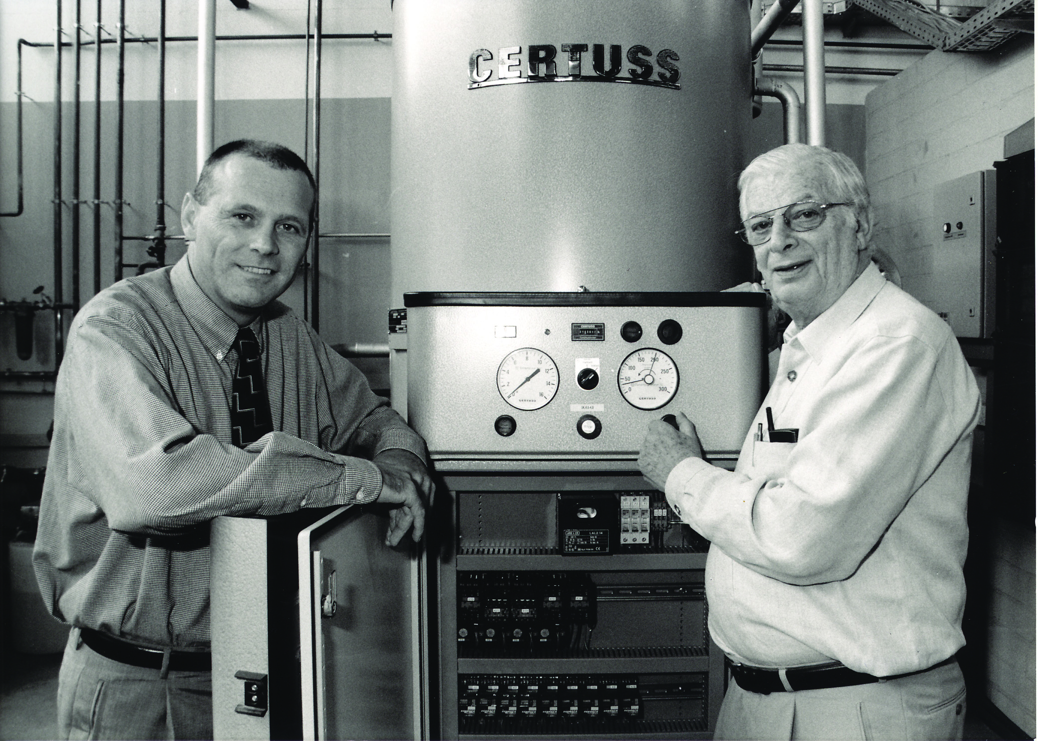 Black and white photo of two people in front of an old steam generator